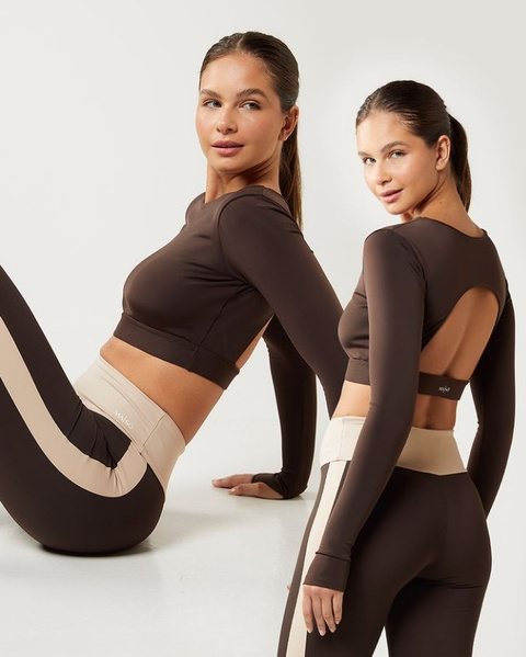 Duas modelos sentadas com conjuntos fitness marrons de manga longa e legging com recorte bege